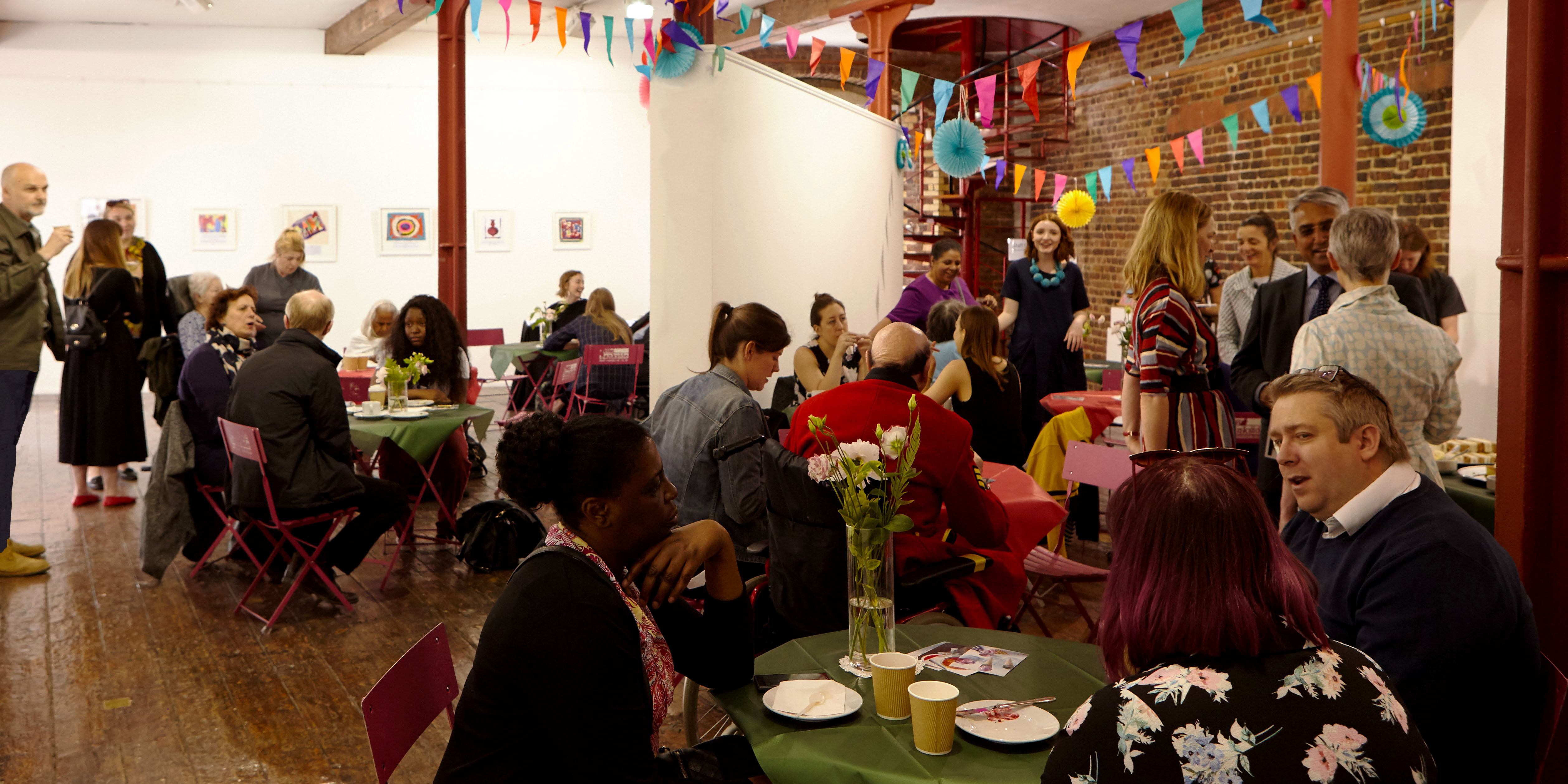 Photo of a cafe space decorated with colourful flags. There are artworrks mounted on the wall in the distance.