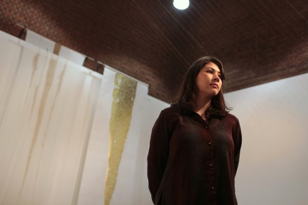 A young woman in dark shirt is wandering in a space with a brown slanted cieling and decorated with white and gold draps