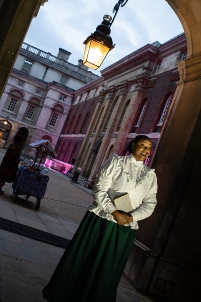 A Black woman wearing a white shirt and green dress holding a book